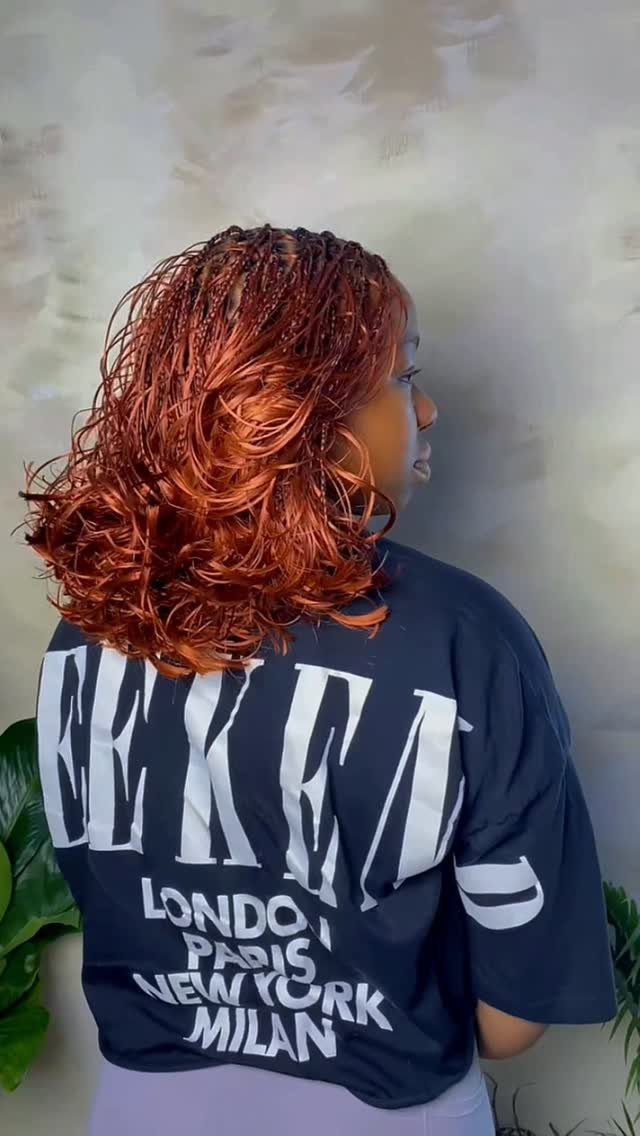 Shoulder-length reddish-brown braids curl over the back of a dark graphic T-shirt