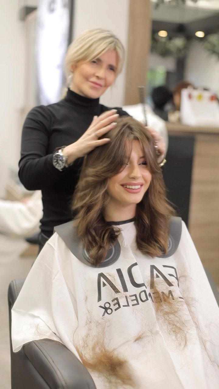 Woman with long brown layered hair and feathered ends in a salon chair