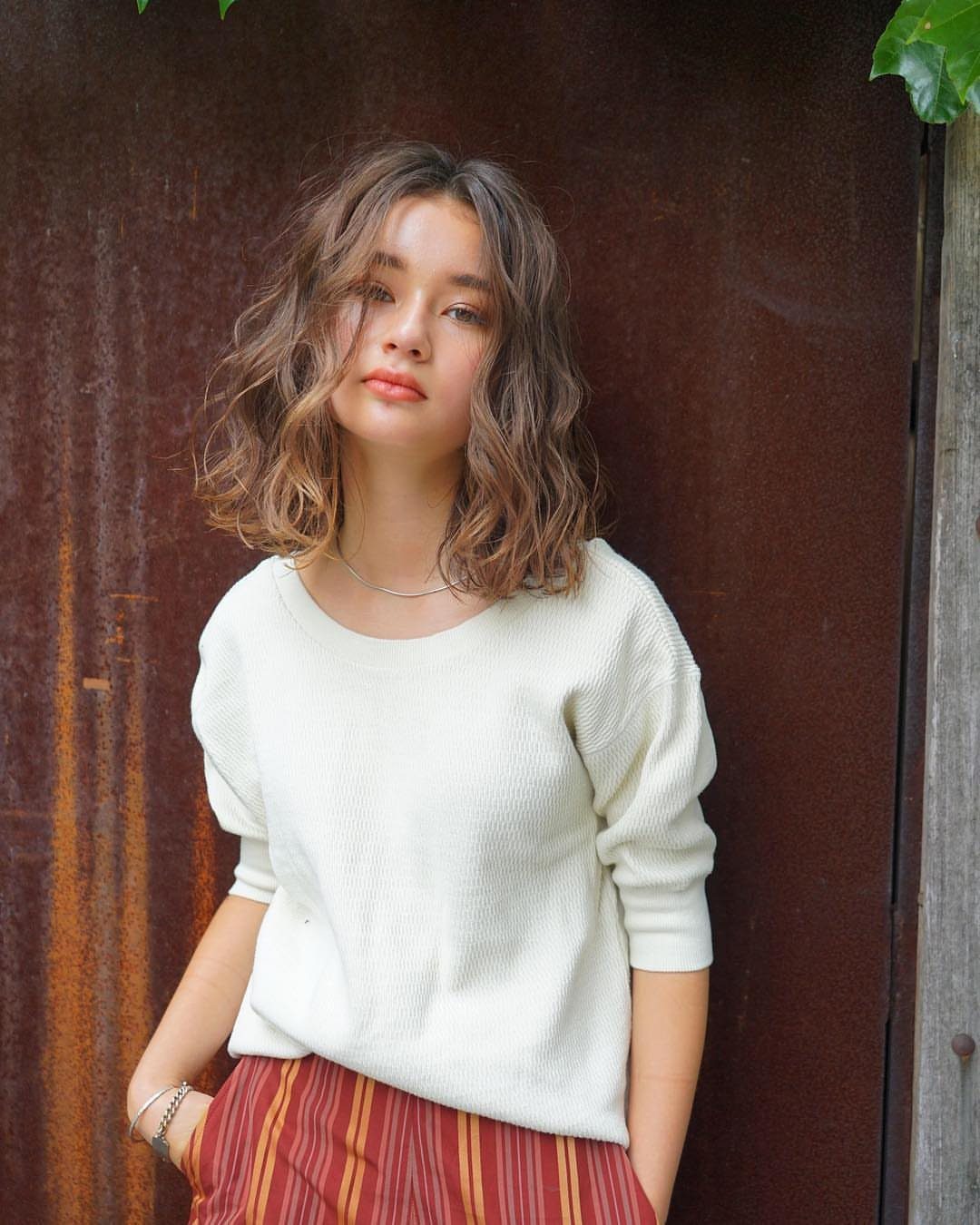 Woman with shoulder-length loose brown waves wearing a white knit top