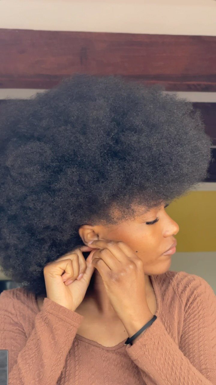 Side-profile person wearing a full rounded natural afro while fastening an earring