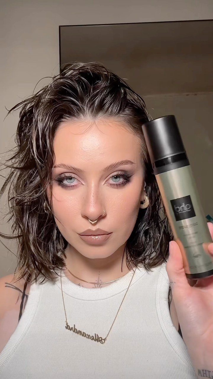 Woman with shoulder-length wet waves holding a hair product beside her face