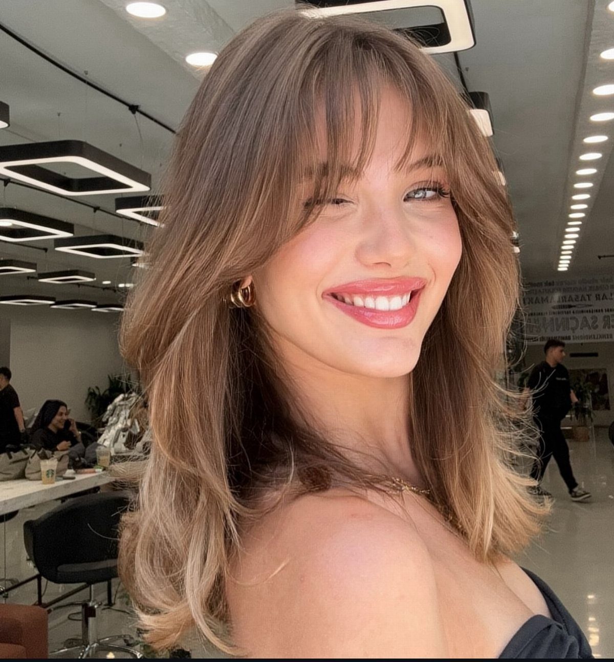 Woman showing shoulder-length brown hair with airy wispy bangs and softly curled ends