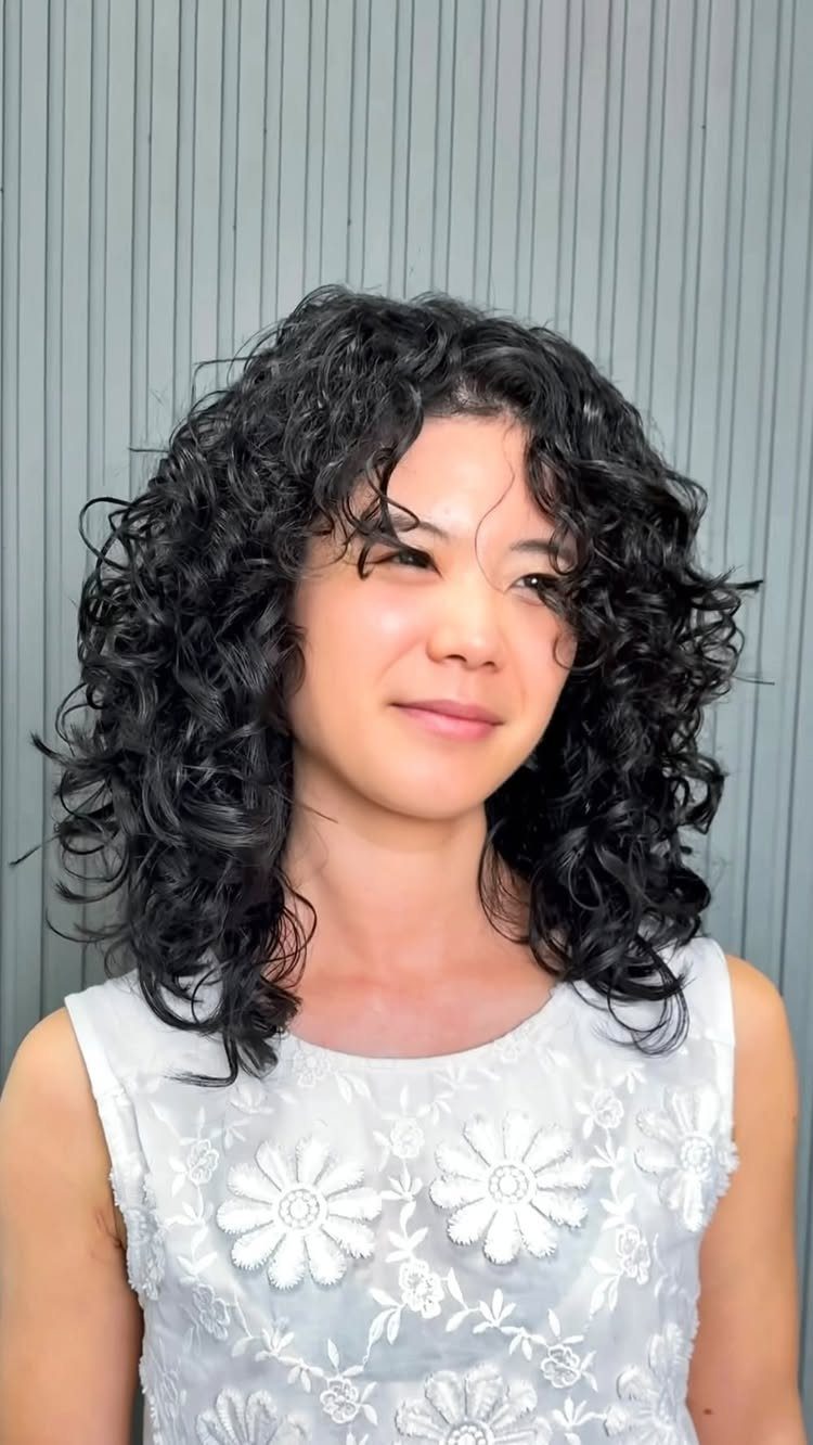 Person with dark shoulder-length curls wearing a white floral sleeveless top