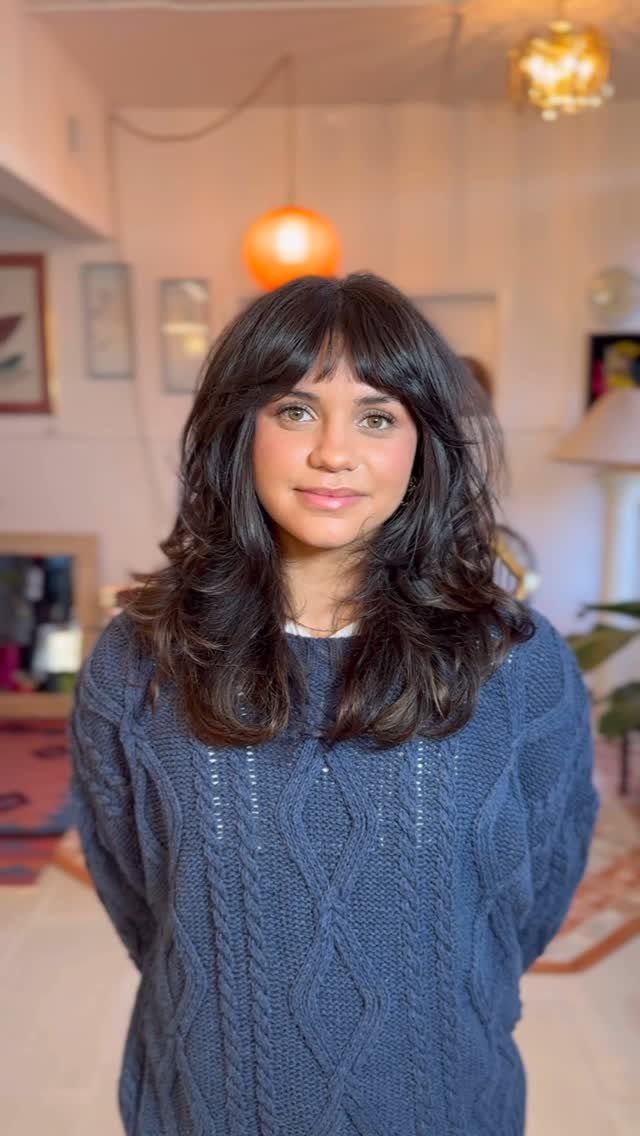 Woman with shoulder-length dark hair and curtain bangs wearing a blue sweater