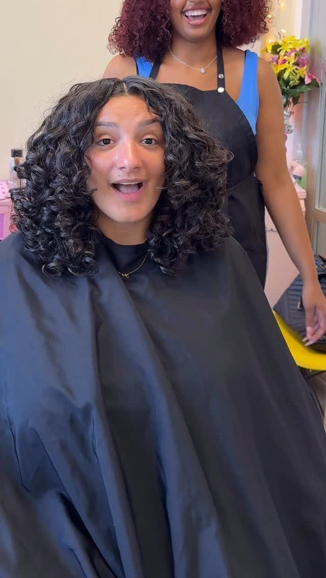 Person with full shoulder-length dark curls seated in a salon chair