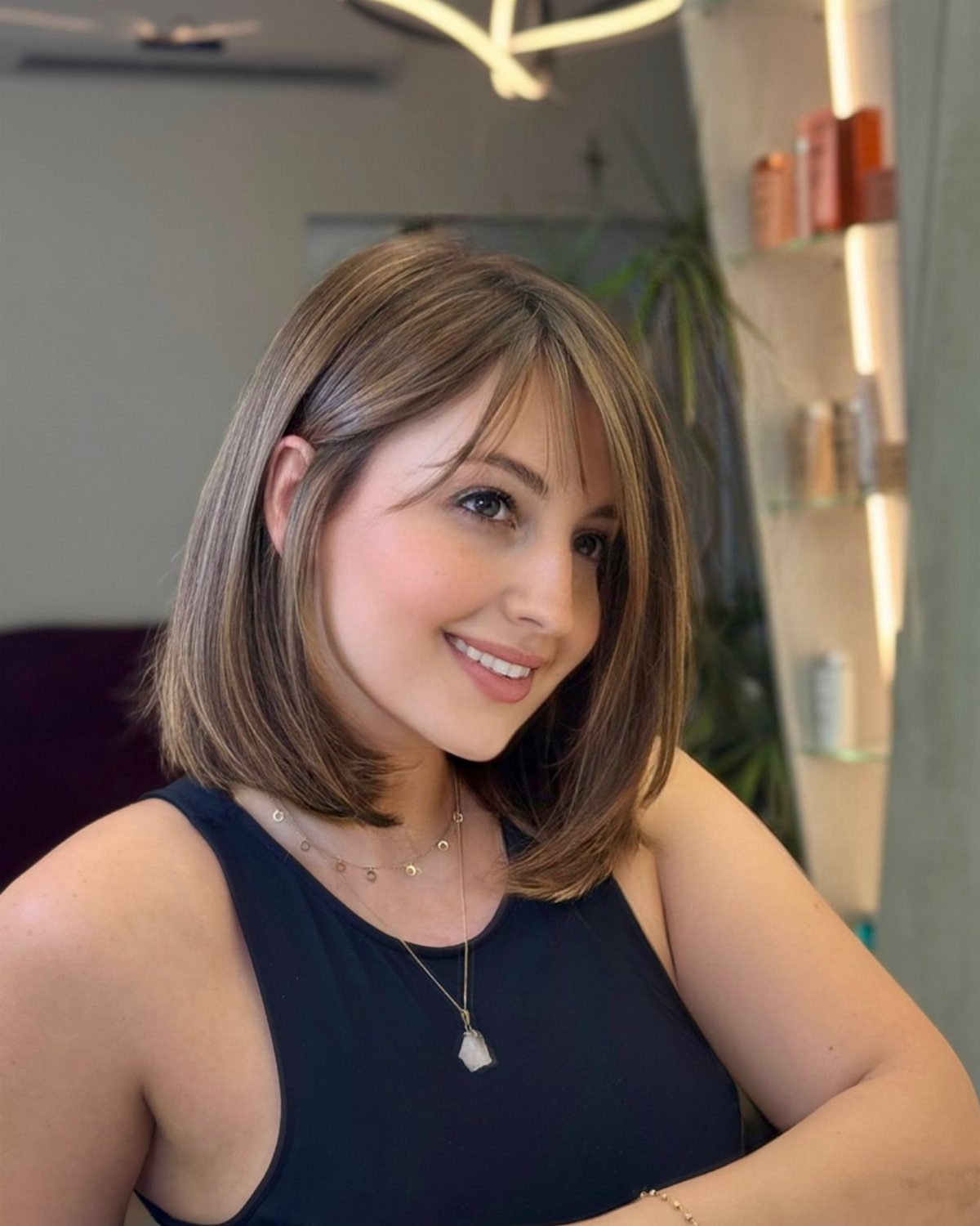 Woman smiling with a rounded shoulder-length brown bob and side-swept bangs