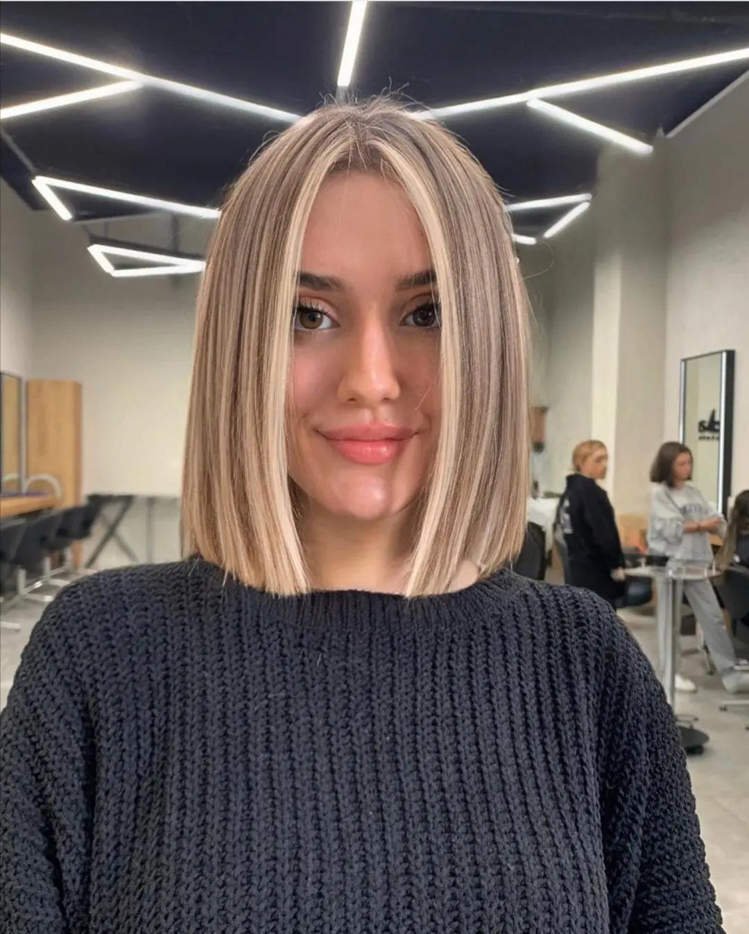Woman with a straight, center-parted blonde bob posing in a hair salon.