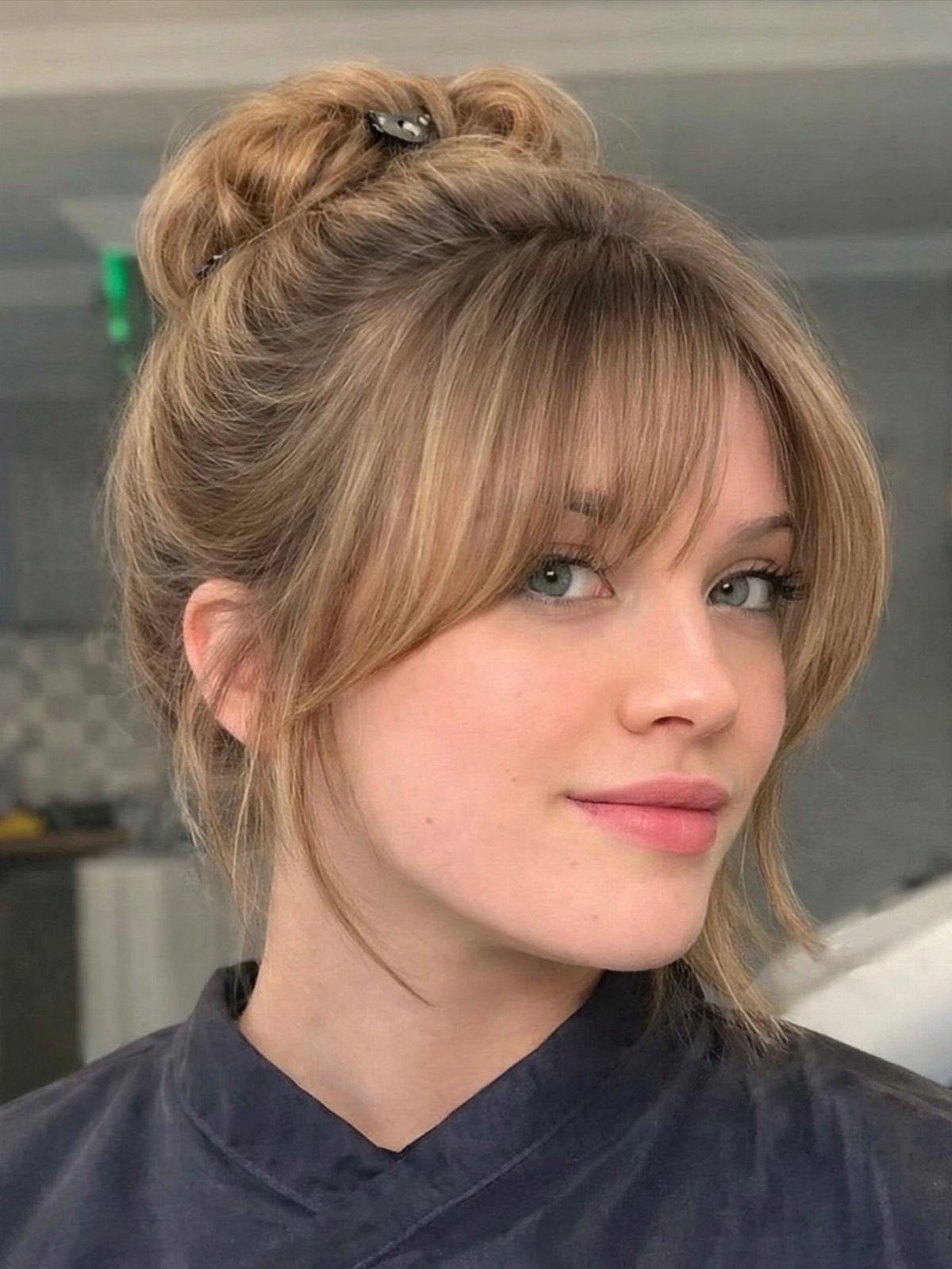 Woman with a high bun and long wispy bangs swept across her forehead
