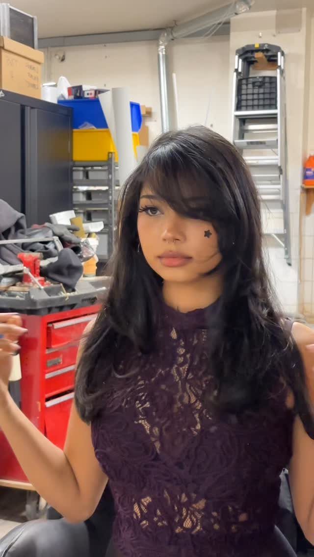 Woman with long dark hair and swoopy side-swept bangs in a workshop