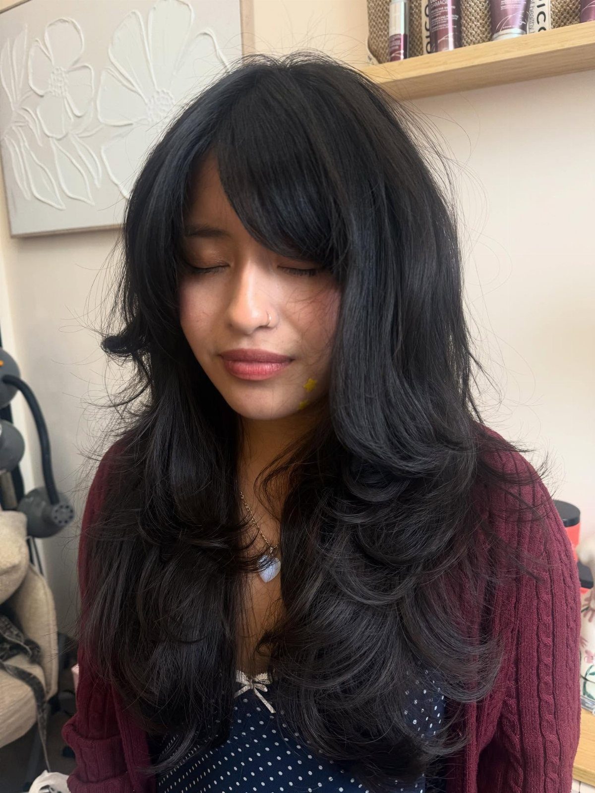 Woman with long layered black hair and side-swept bangs indoors