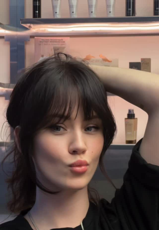 Young woman wears tousled, choppy dark bangs with layered shoulder-length hair