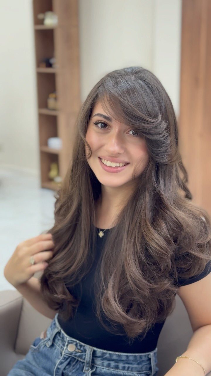 Woman with voluminous layered brown hair, waves, and side-swept bangs