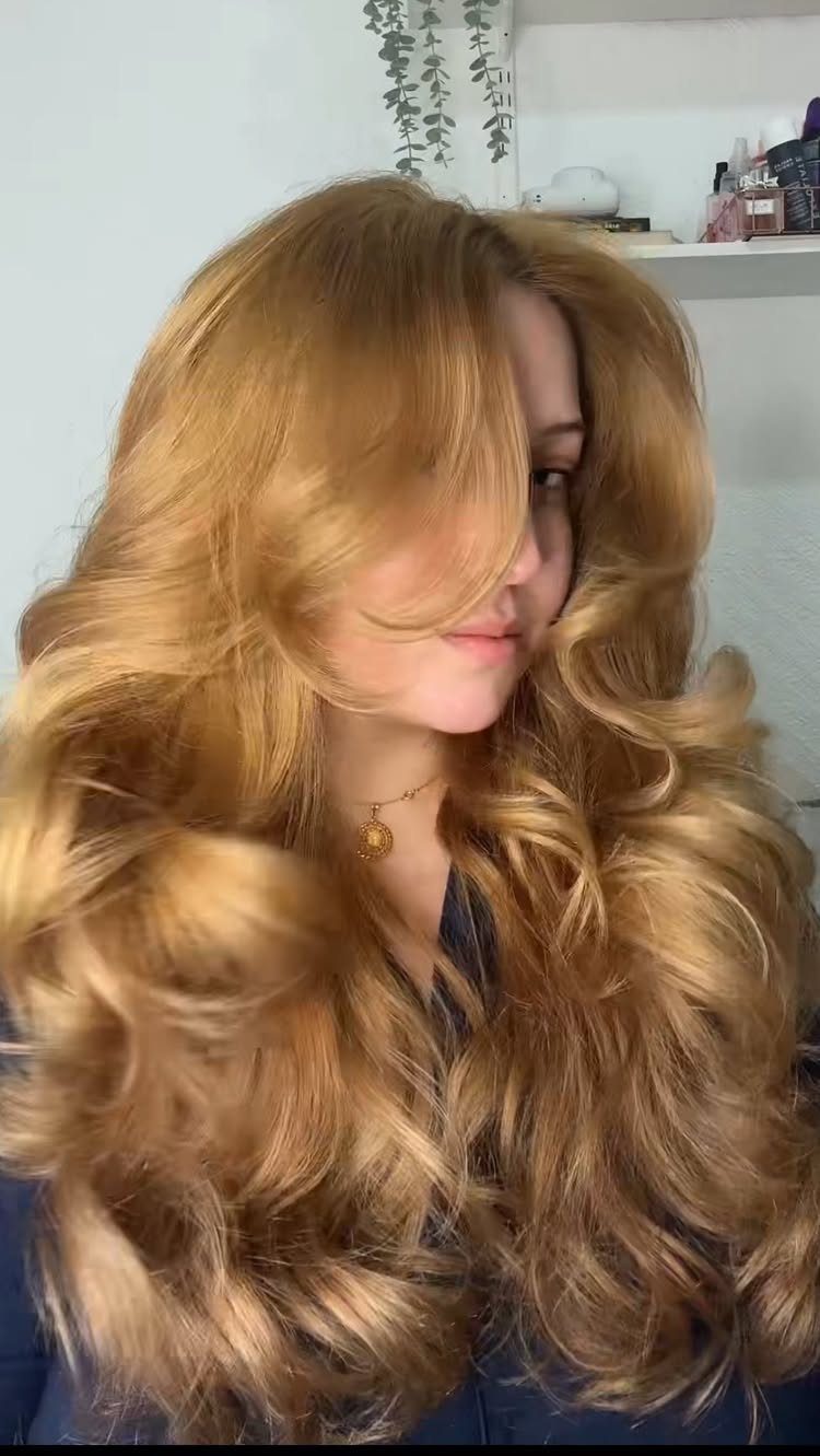 Long golden-blonde hair styled in voluminous, bouncy waves with a side part