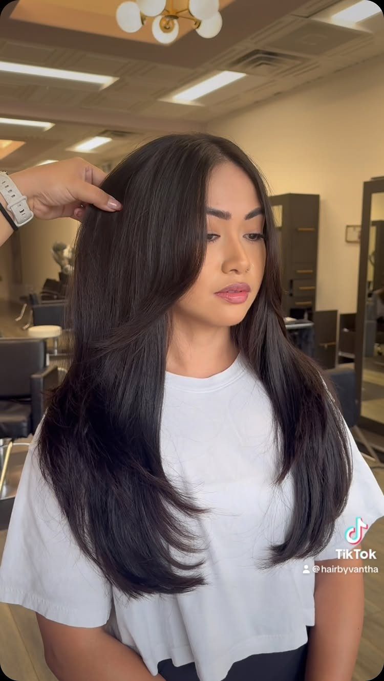 Woman with long dark hair and curtain bangs seated in a salon chair