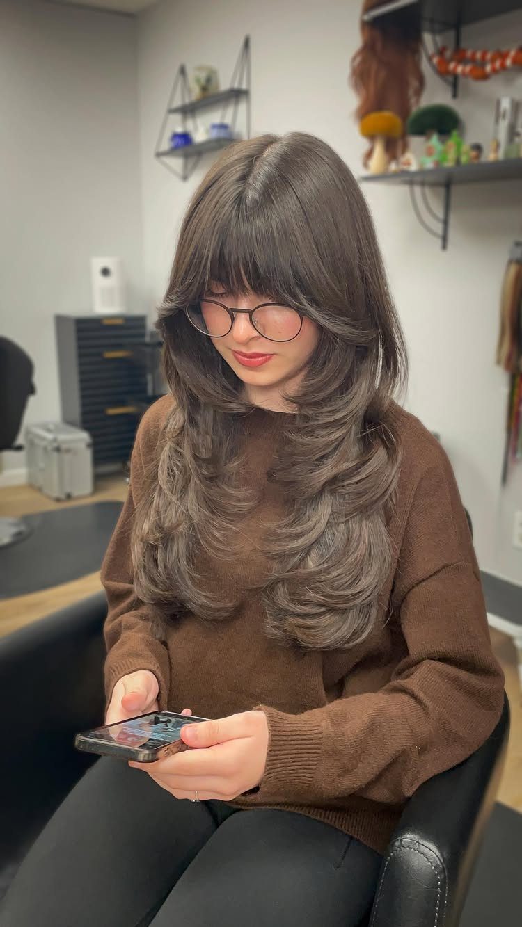 Woman with long brown layers and outward-flipped ends seated in a salon