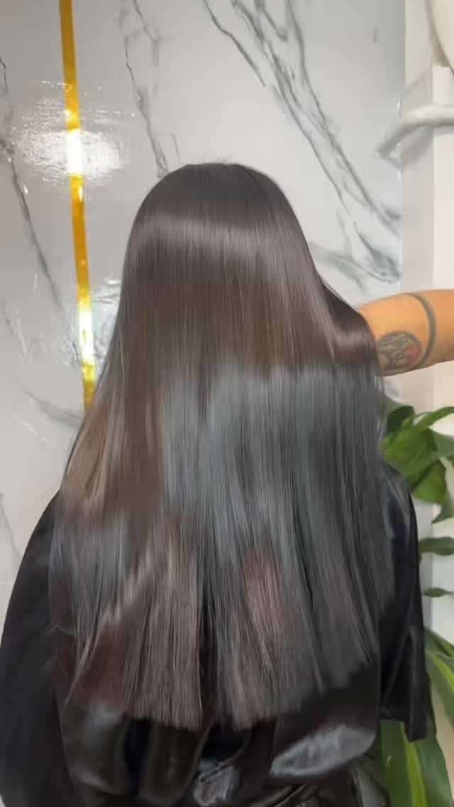 Long glossy straight dark hair falls smoothly over a black salon cape