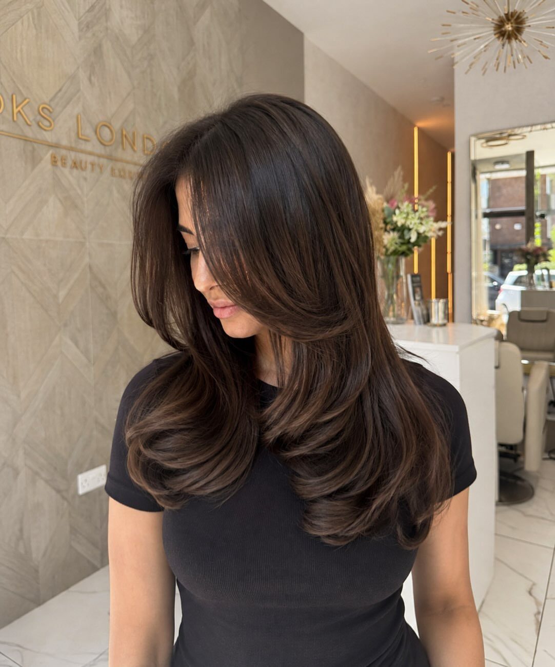 Woman with long, dark layered hair styled with smooth, curled ends in a salon