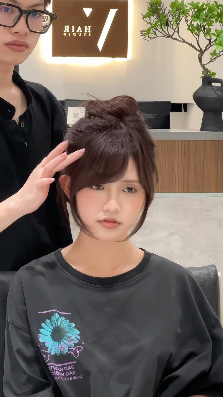 Woman with a high bun and wispy side-swept bangs at a salon