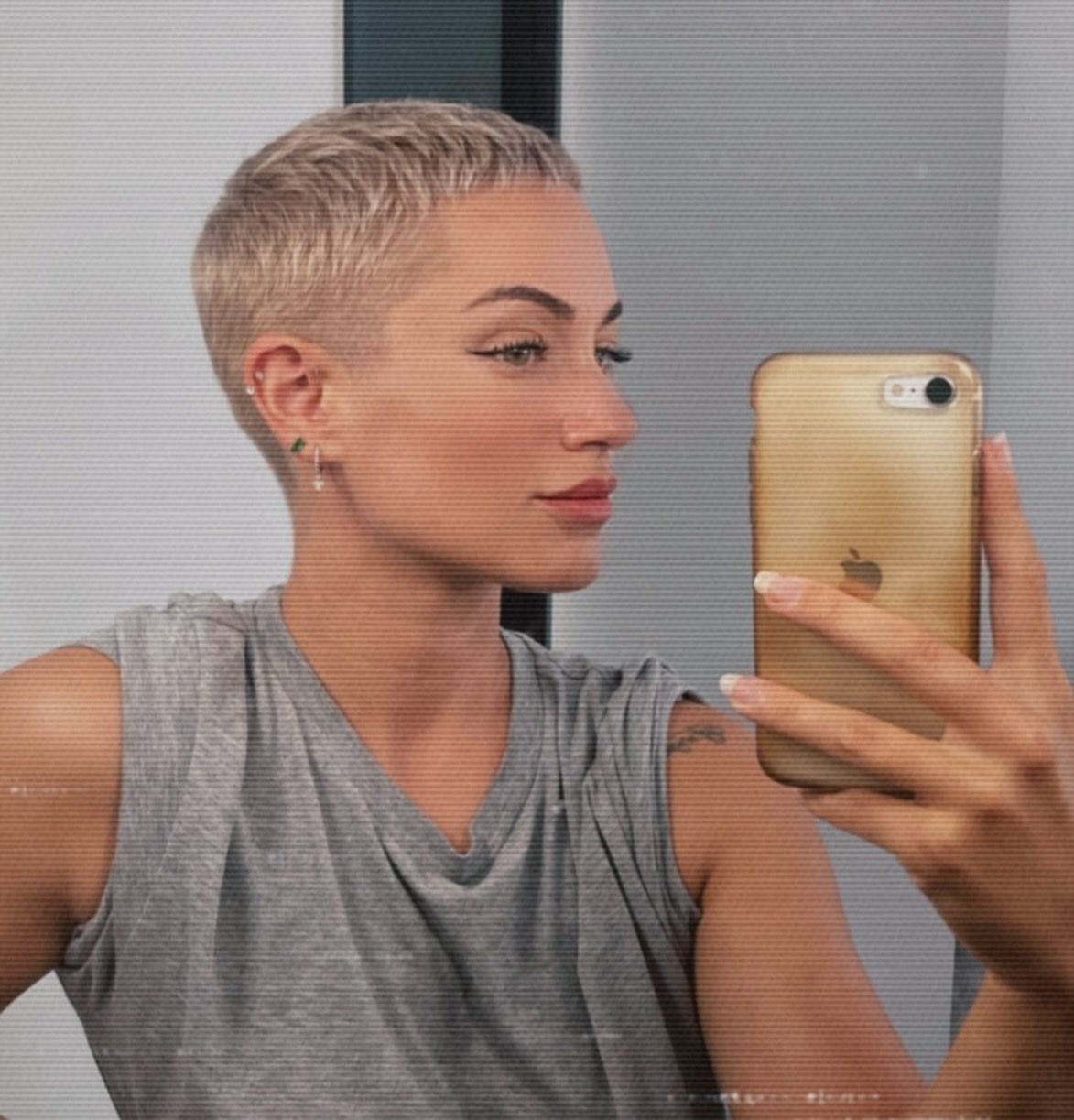 Person with a short textured blonde pixie haircut taking a mirror selfie