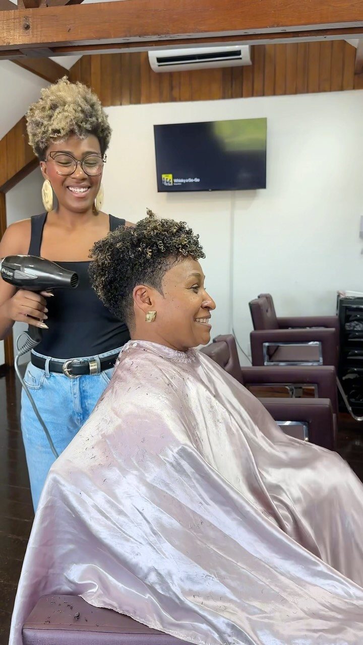 Client with short curly hair and tapered sides seated under a silver barber cape