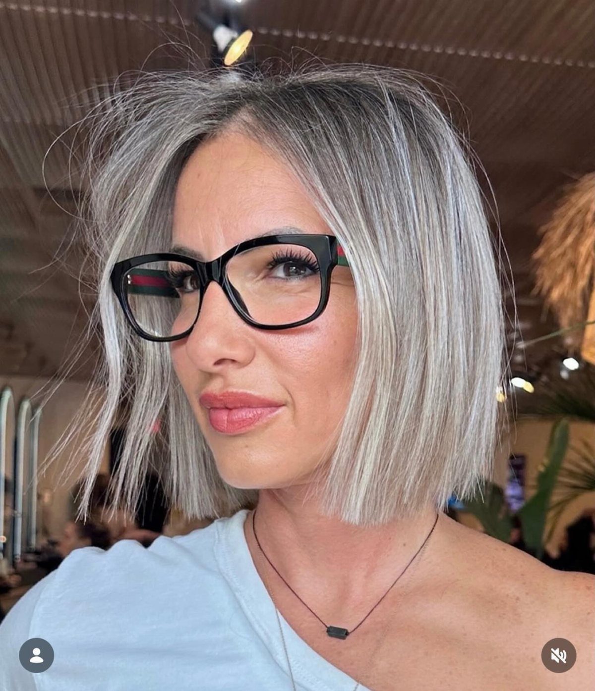 Woman with silver-gray hair wearing a straight, chin-length blunt bob and black glasses