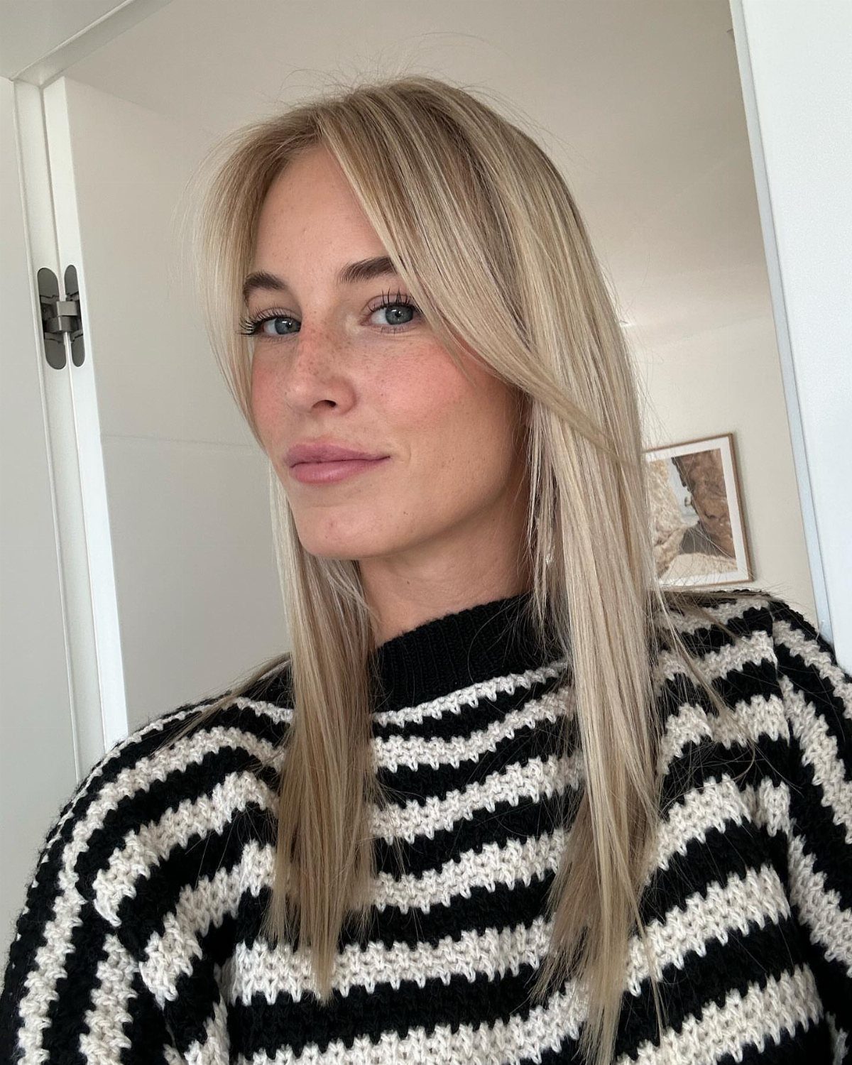 Woman with long blonde curtain bangs wearing a striped knit sweater
