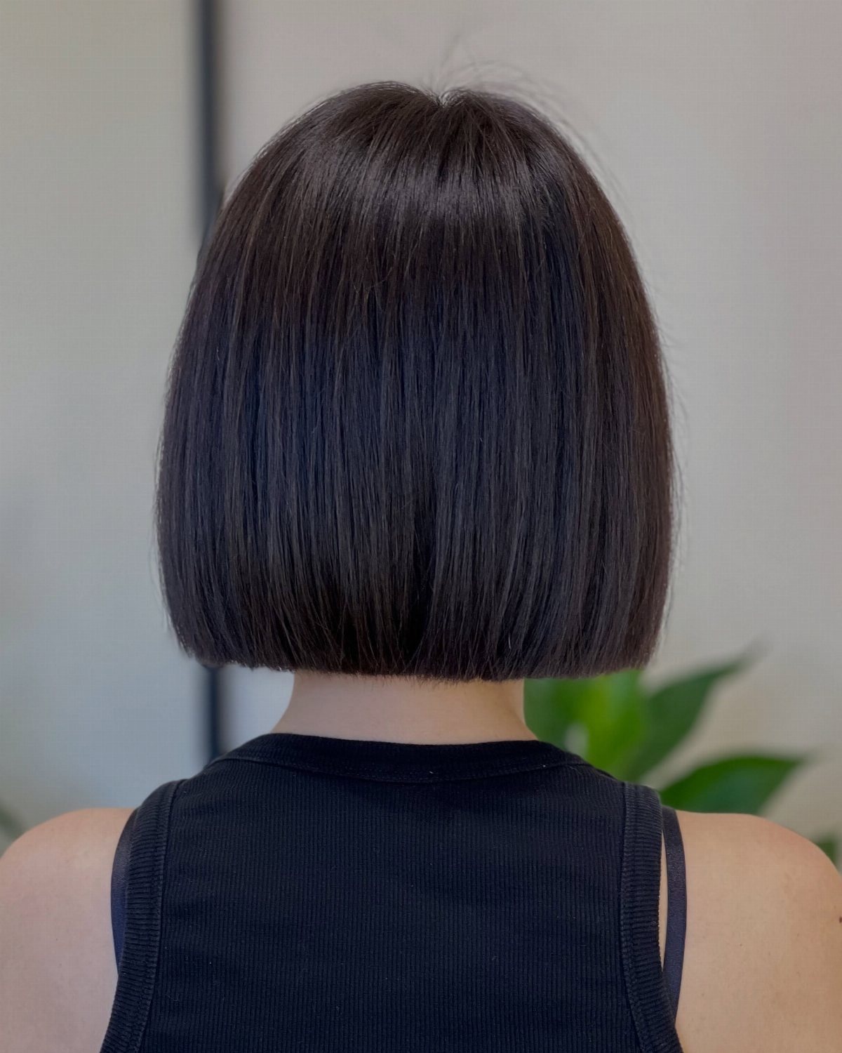 Dark blunt chin-length bob viewed from behind against a pale indoor wall