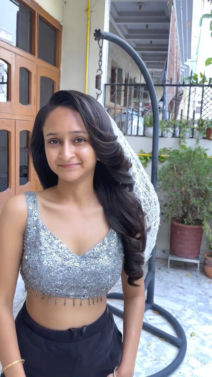 Woman with long dark curls swept over one shoulder in a silver top