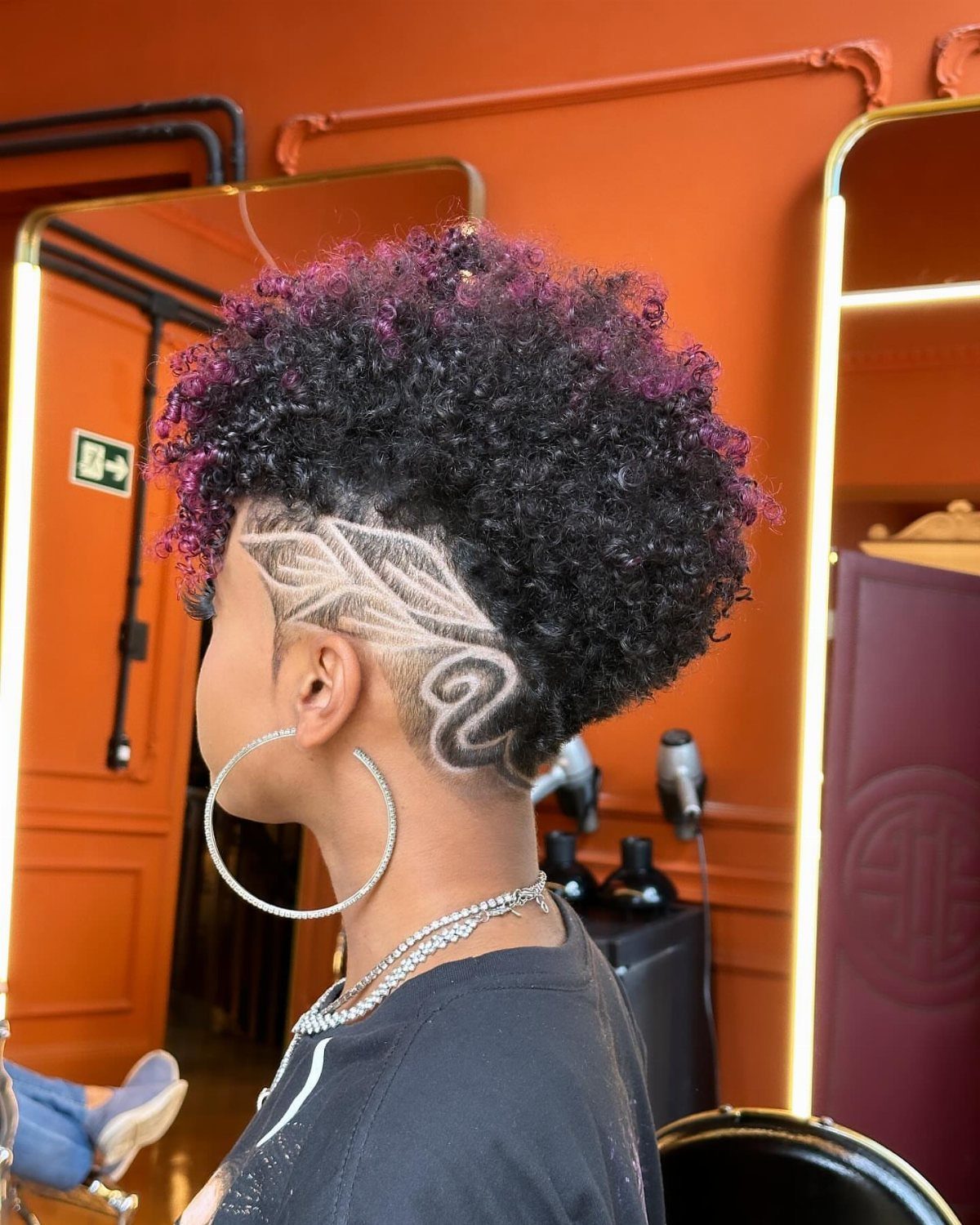 Curly high-top hairstyle with shaved sides and curved designs in a salon