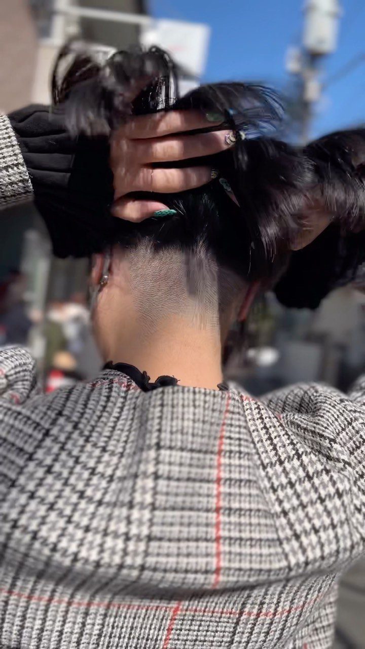 Gloved hands lift long black hair to reveal a closely shaved undercut